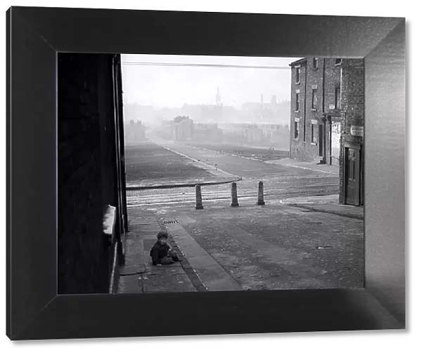 A photograph of a child sitting on the pavement in a Liverpool slum housing area