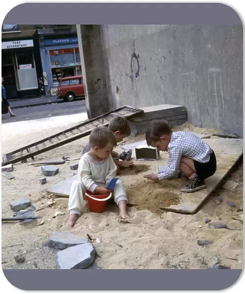 Three boys playing with sand in a Balham street, SW London