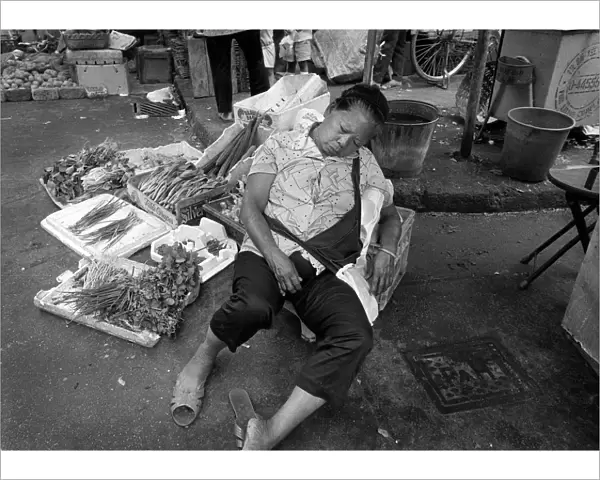 A woman sleeps at her vegetable stall in a Hong Kong market