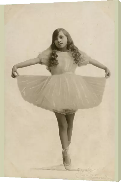 A Young Ballerina with long curled hair on point, holding out her tutu - studio portrait