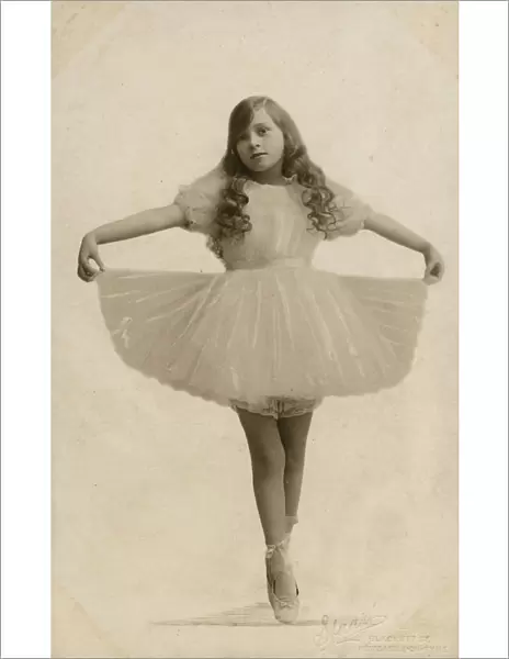 A Young Ballerina with long curled hair on point, holding out her tutu - studio portrait