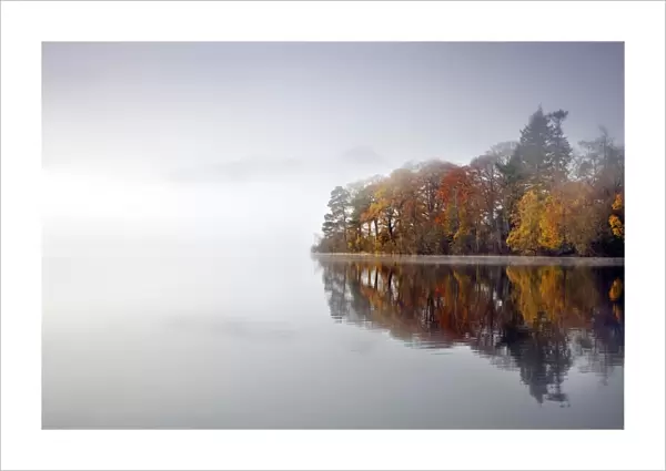 Derwent Water - autumn colours reflected in water of derwent island in the mist with catsbells just visable through the mist - Lake District - England