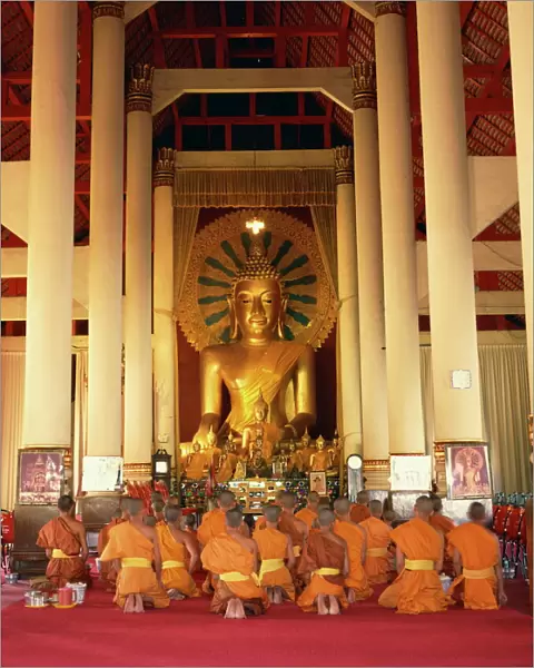 Monks in saffron robes kneel before a statue of the