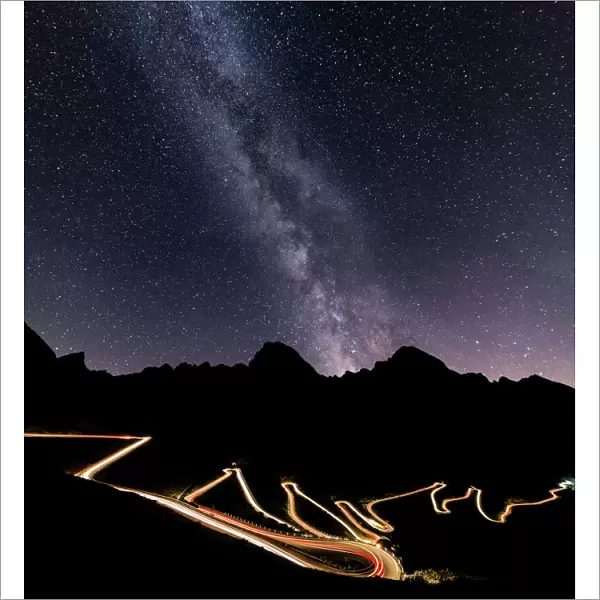 Panorama of the Milky Way and lights of car trace at Stelvio Pass, Valtellina, Lombardy