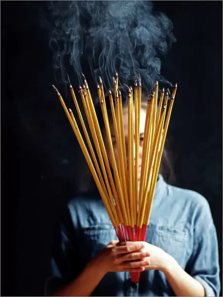 Young Chinese woman praying with big burning incense sticks in her hands