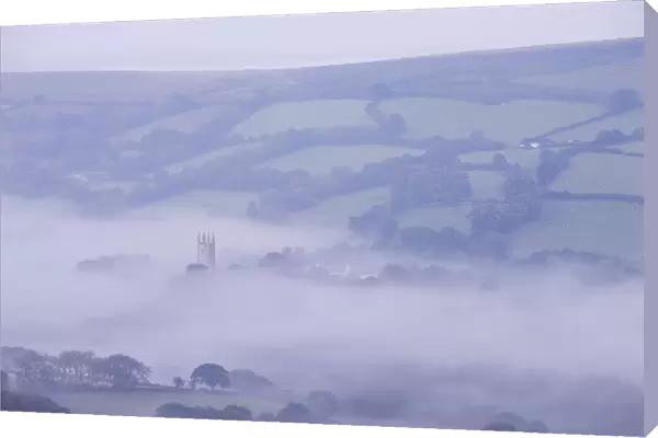 Morning mist swirls around the church tower of Widecombe in the Moor, Dartmoor, Devon