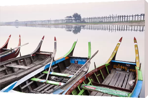 Traditional Burmese boats at sunrise on Taungthaman Lake with U Bein Bridge in the