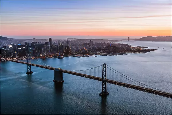 Aerial of downtown district at sunset with Bay bridge in the foreground, San Francisco