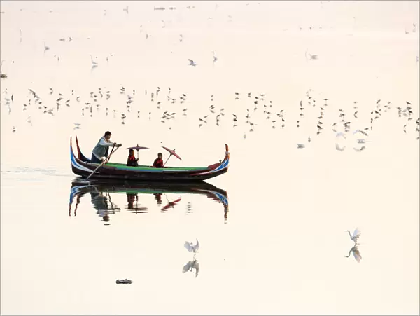 A rowing boat surrounded by birds carries two novice monks towards U-Bein bridge