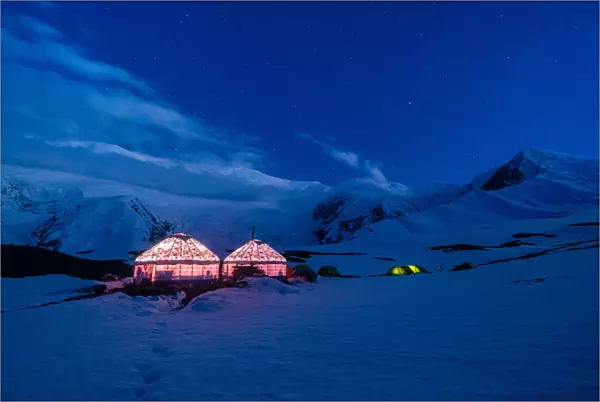 The yurts and tents of peak Lenin camp one illuminated at dusk with Peak Lenin massif in