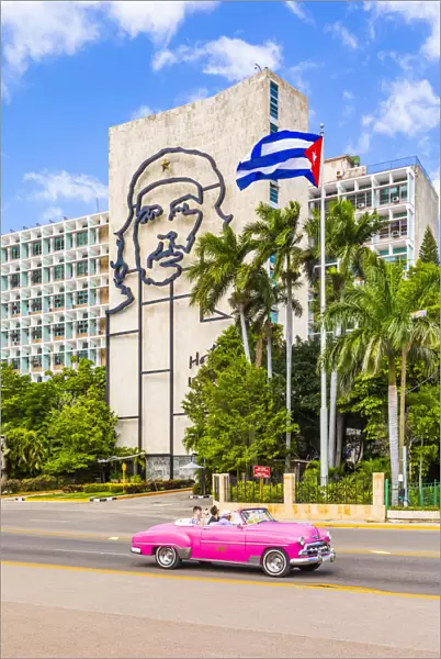A classic car driving in front of a building with an outline of Che Guevara