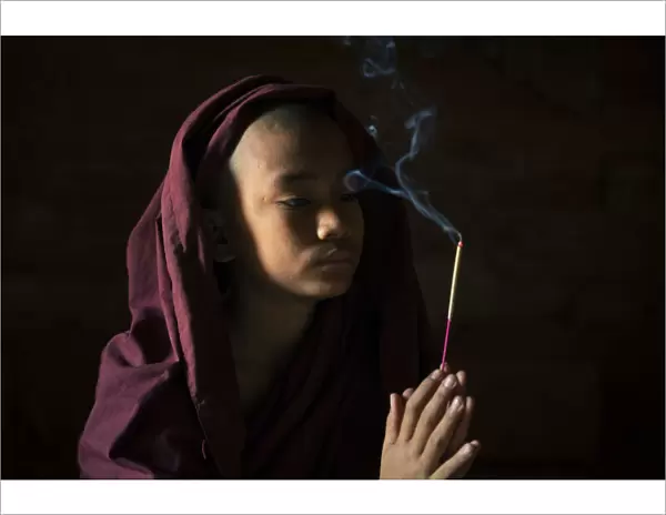 Novice monk holding a lit incense stick while praying inside a temple, UNESCO, Bagan