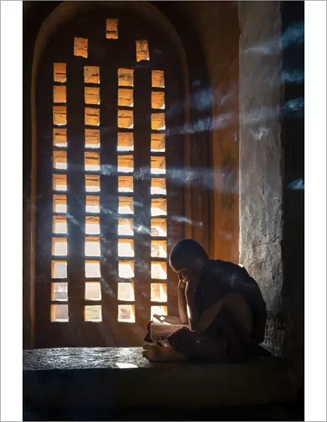 A young monk studying by a window inside a temple, UNESCO, Bagan, Mandalay Region