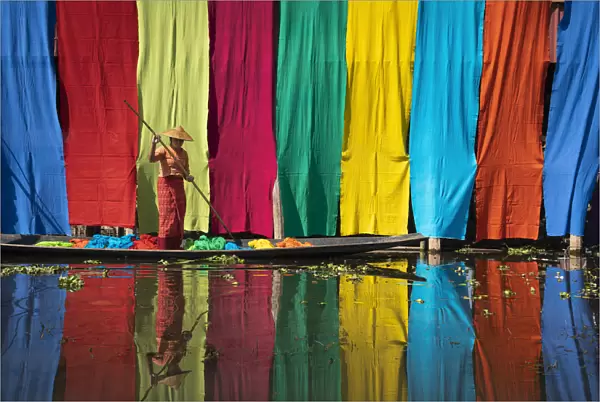 Woman on a boat checking freshly dyed fabric hanging from bamboo poles to dry