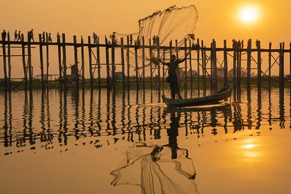 Fisherman throwing fishing net at Taungthaman Lake against U Bein bridge at sunset