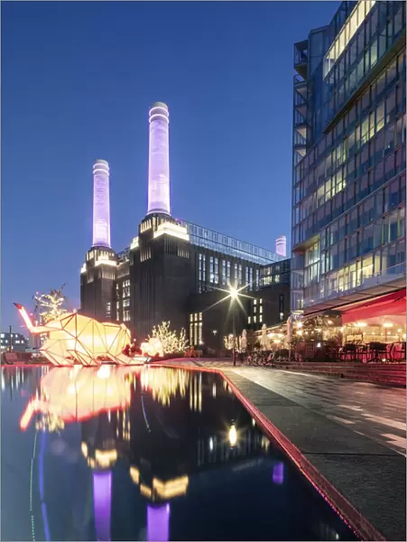 UK, England, London, Borough of Wandsworth. Night view of Battersea Power Station (architects: Leonard Pearce & Giles Gilbert Scott, 1929-19350 & modern retail and residential buildings by Frank Gehry)