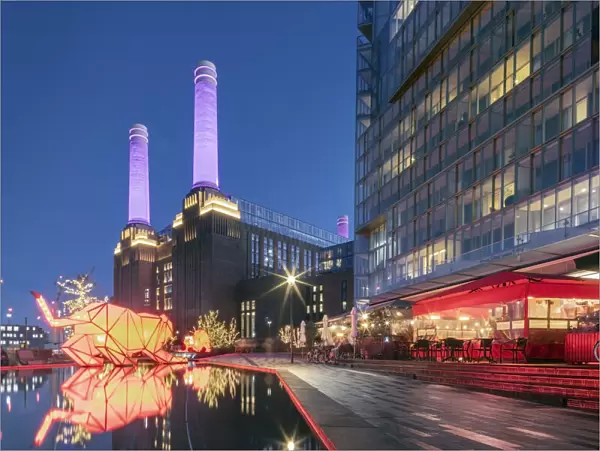 UK, England, London, Borough of Wandsworth. Night view of Battersea Power Station (architects: Leonard Pearce & Giles Gilbert Scott, 1929-19350 & modern retail and residential buildings by Frank Gehry)