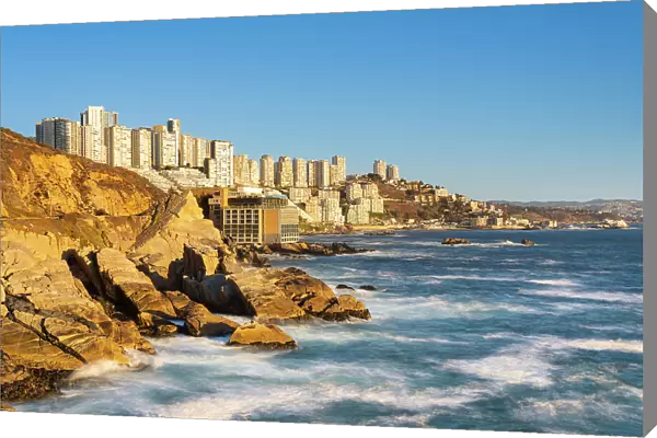 Rocky coastline by Roca Oceanica with distant view of residential high-rise buildings in Renaca, Concon, Valparaiso Province, Valparaiso Region, Chile