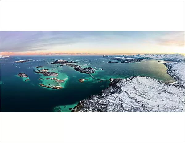 Panoramic aerial view of Sommaroy island in between snowy mountains and frozen sea at dawn, Troms county, Norway