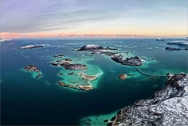 Panoramic aerial view of Sommaroy island in between snowy mountains and frozen sea at dawn, Troms county, Norway