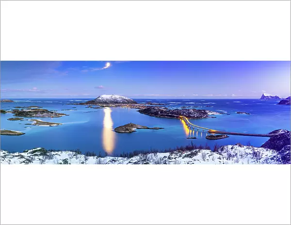 Panoramic view of Sommaroy bridge along a frozen fjord lit by moon at dusk, Troms county, Norway