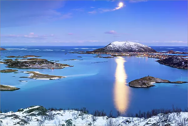 Panoramic view of Sommaroy bridge along a frozen fjord lit by moon at dusk, Troms county, Norway