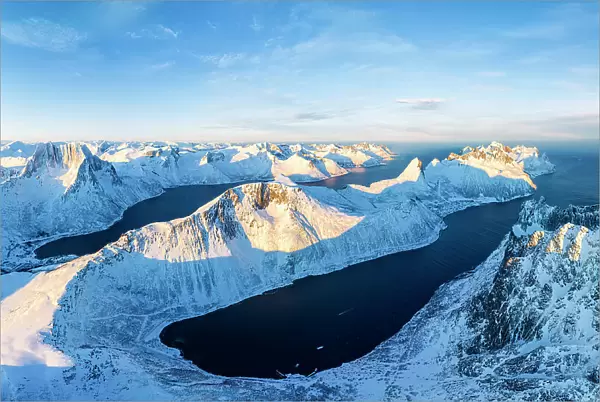 Aerial view of the snowy Barden, Segla, Breidtinden mountains overlooking the icy Mefjorden and Ornfjord, Senja, Troms, Norway