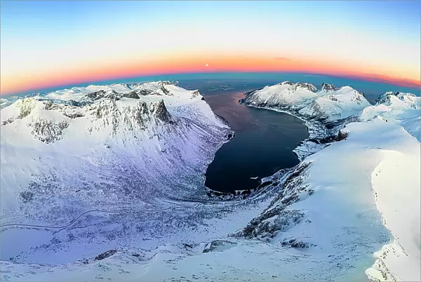 Panoramic aerial view of frozen fjord and majestic snowy mountains surrounding Bergsfjord at dawn, Senja, Troms county, Norway