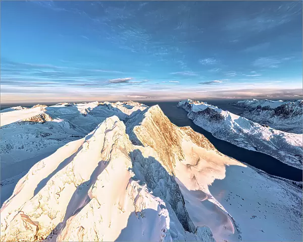 Dramatic sky at dawn over majestic Breidtinden mountain peak covered with snow, aerial view, Mefjorden, Senja, Troms county, Norway