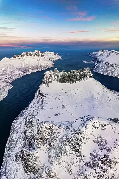 Romantic sunrise over the snowy peak of Grytetippen mountain along the icy sea, aerial view, Ornfjord, Senja, Troms, Norway