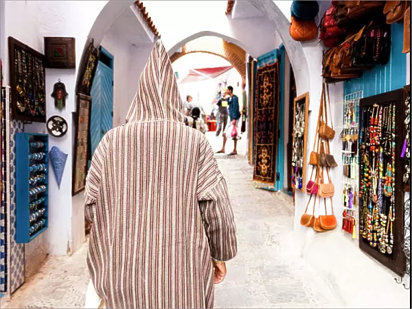 Man with traditional Djellaba looking at the gift shops in the street markets of Chefchaouen, Morocco