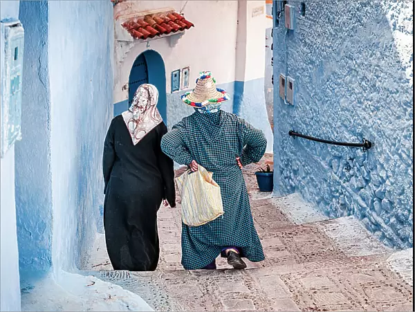 Senior women with hijab walking along the blue buildings of medina, Chefchaouen, Morocco