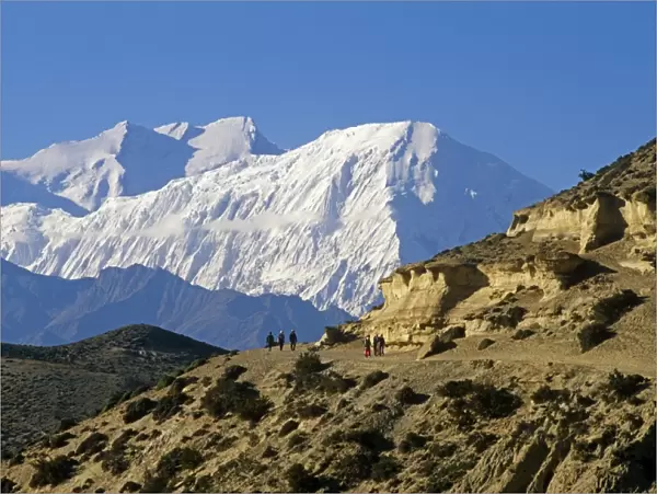 Nepal, Himalaya, Mustang. Trekkers on the main Mustang trail with the Annapurna massif soaring on the