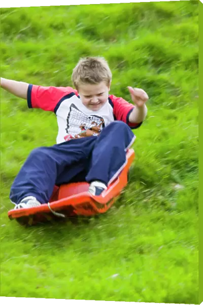 A young boy sledging down a grassy bank
