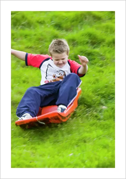 A young boy sledging down a grassy bank