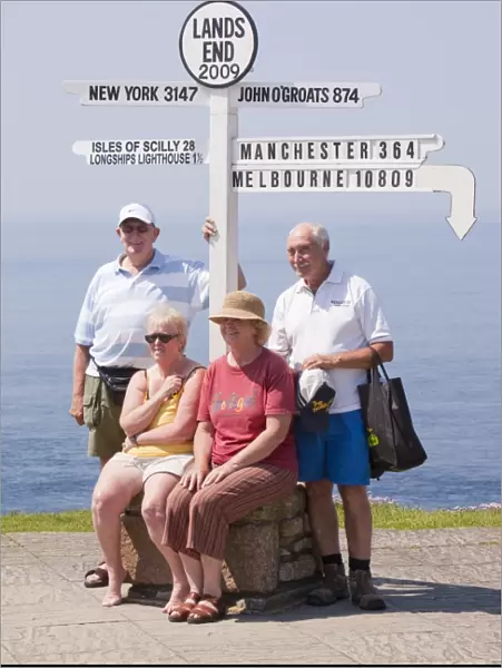 Friends on holiday having their photo taken at Lands End with the distance to the town where they live