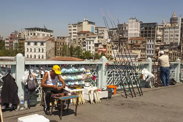 Turkey, Istanbul, Man fishing and man selling fishing tackle on Galata Bridge