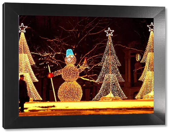 A man walks in past illuminated installations in the shape of a snowman and Christmas