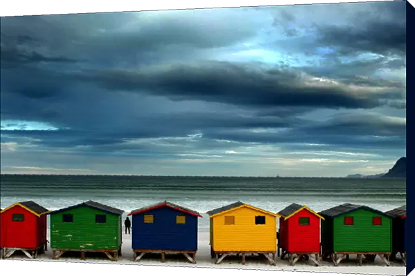LONE STROLLER STANDS BY BEACH HUTS IN CAPE TOWN