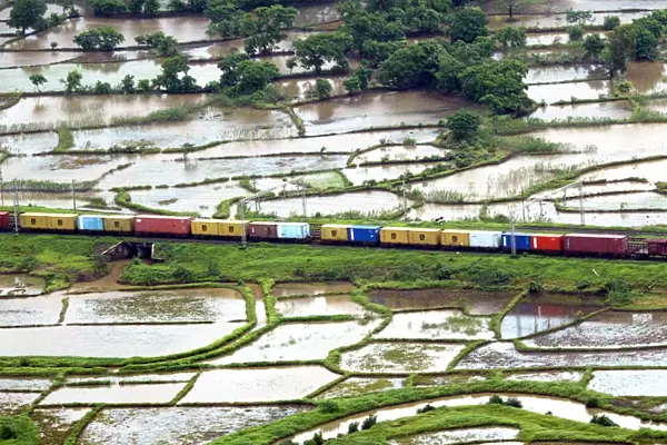 An aerial view of a train passing through a track surrounded by vast expanse of farmlands