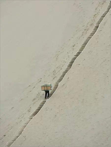 A worker carries sleds up the Mingsha Sand Dunes on the outskirts of Dunhuang