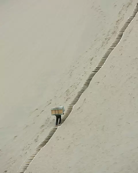A worker carries sleds up the Mingsha Sand Dunes on the outskirts of Dunhuang