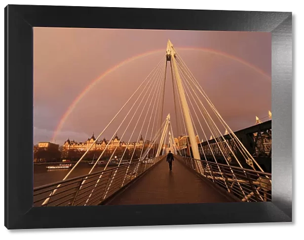 A rainbow appears as a pedestrian crosses one of the Golden Jubilee Bridges in London