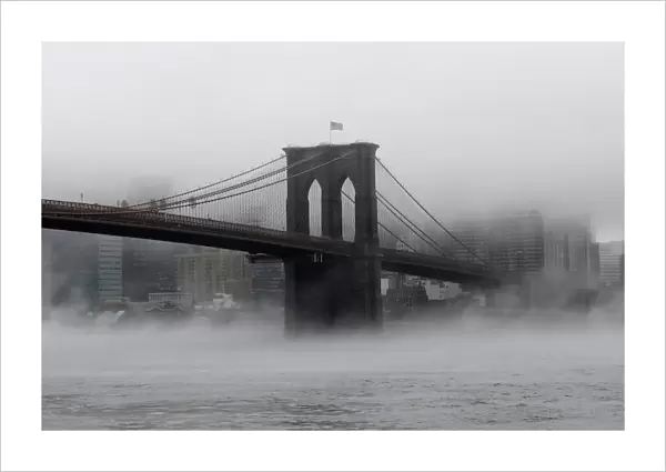 The Brooklyn Bridge is seen partially in fog from in front of the Manhattan skyline