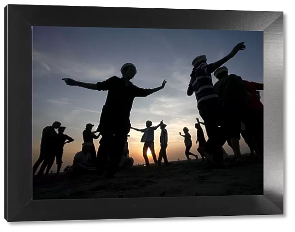 Men are silhouetted as they dance to celebrate during sunset at a beach in Karachi