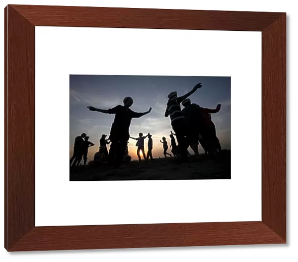 Men are silhouetted as they dance to celebrate during sunset at a beach in Karachi