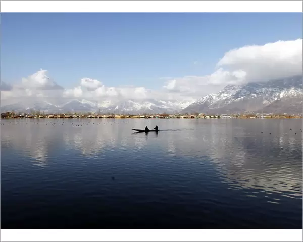 A man rows a small boat on the waters of Dal Lake on a sunny day in Srinagar