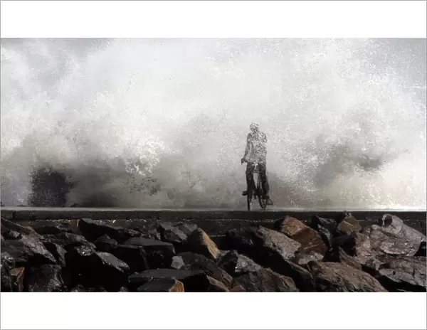 A man is drenched by a large wave during high tide as he cycles past at a fishing