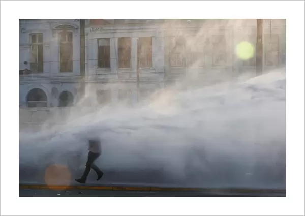 Chilean dockworkers are sprayed by a riot police water truck during a protest against the