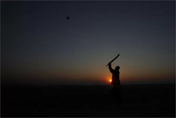 A man is silhouetted against the setting sun as he plays cricket at a park in Lahore